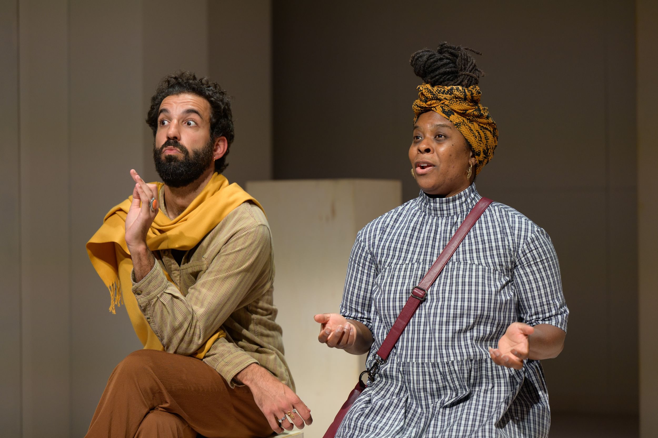 Maseda, in a yellow scarf, is poised to interrupt Young, who speaks with palms upturned. She wears a headwrap & plaid dress.