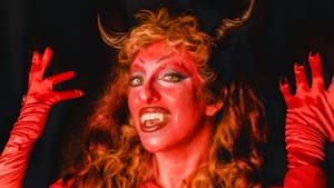 Einbinder in all “devilish” red silk, hair, makeup, horns, posing while revealing their fangs.