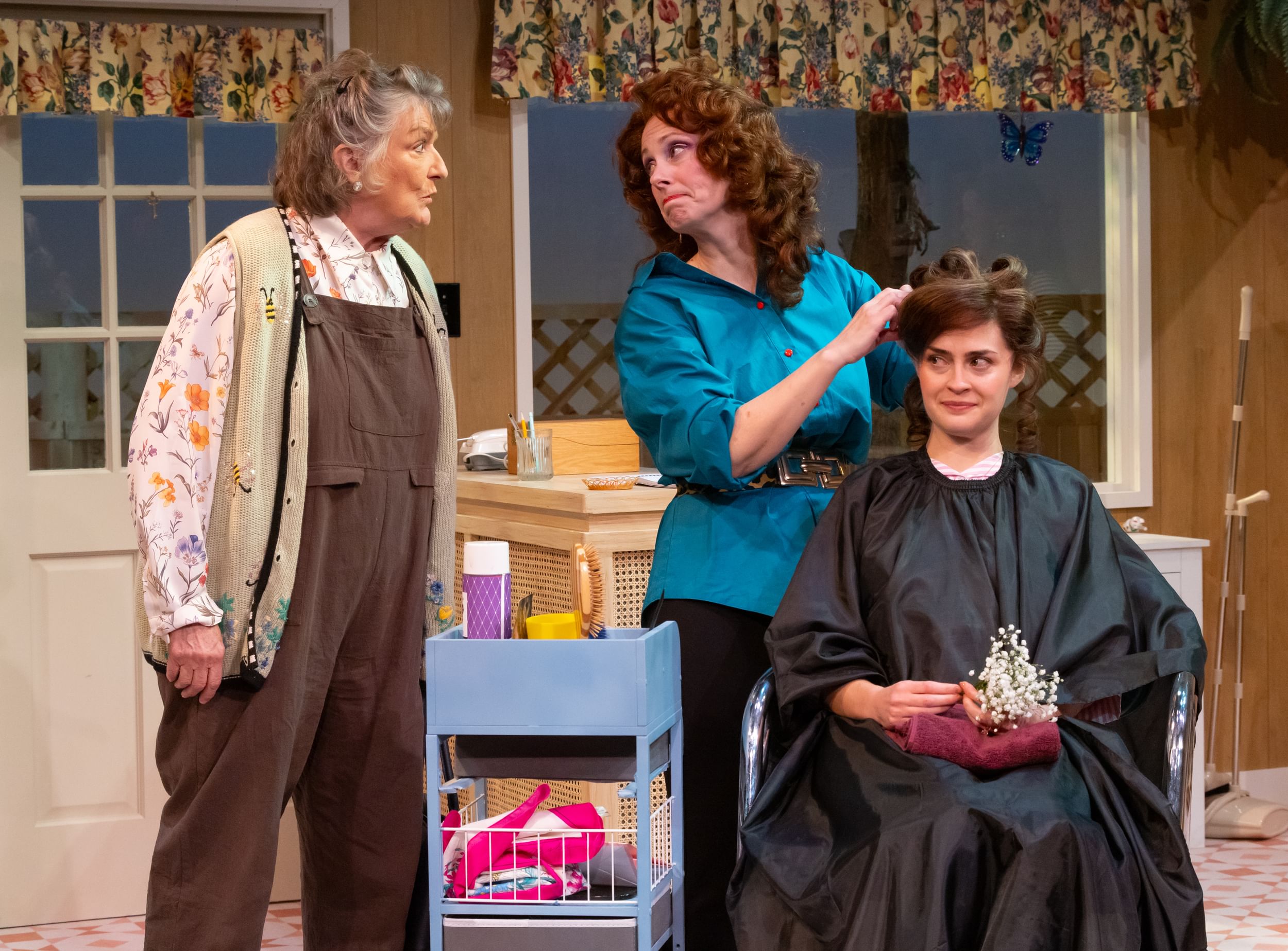 Saunders, with short gray hair and brown overalls, speaks to Lamm, wearing turquoise, who does Inie-Richards’ bouffant updo.