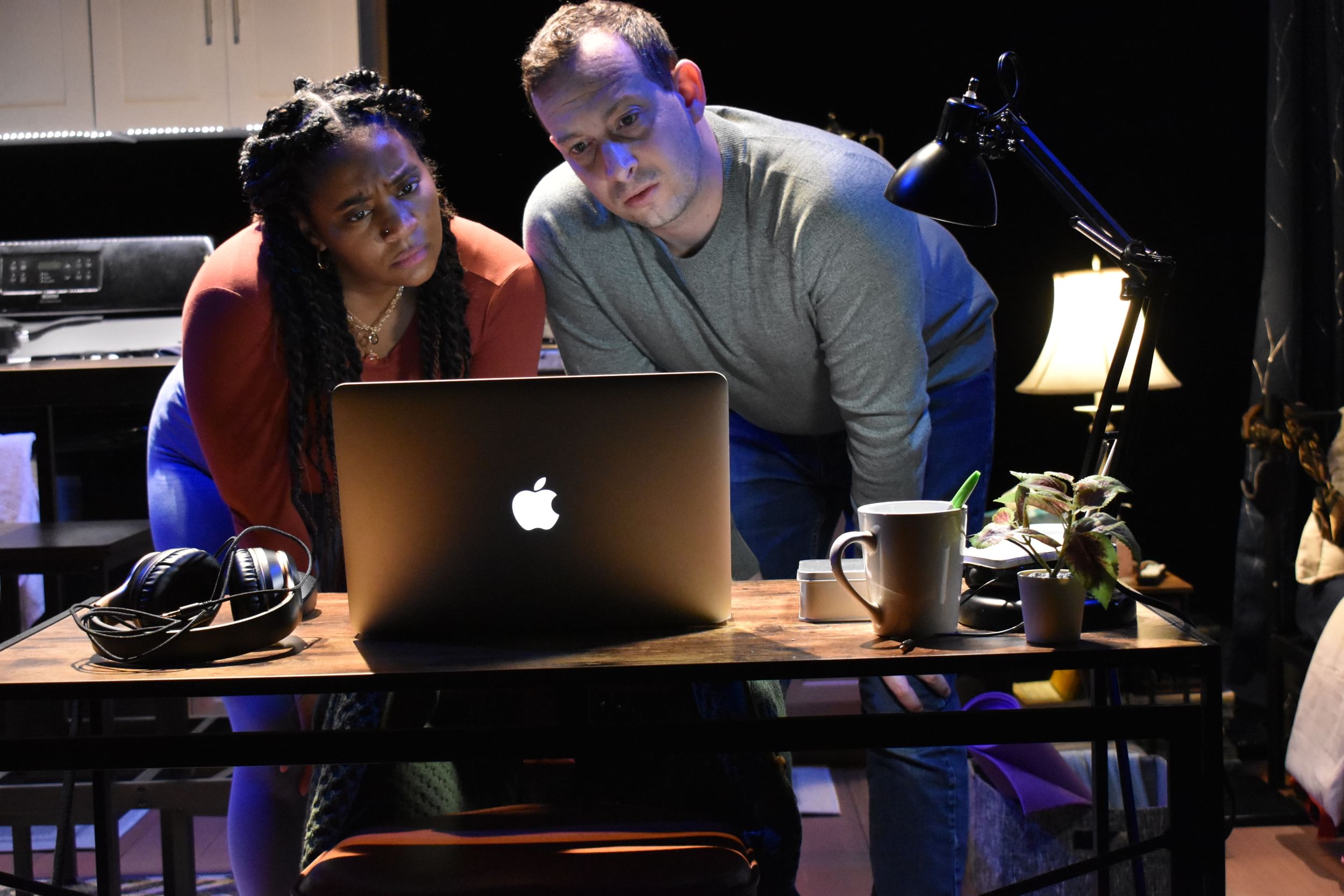 In a darkened apartment, Johnson and Sheppard lean over a laptop screen with skeptical but interested faces.