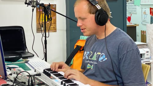 Steven, a young white man, smiling in profile as he works in a small recording studio, wearing a headset.