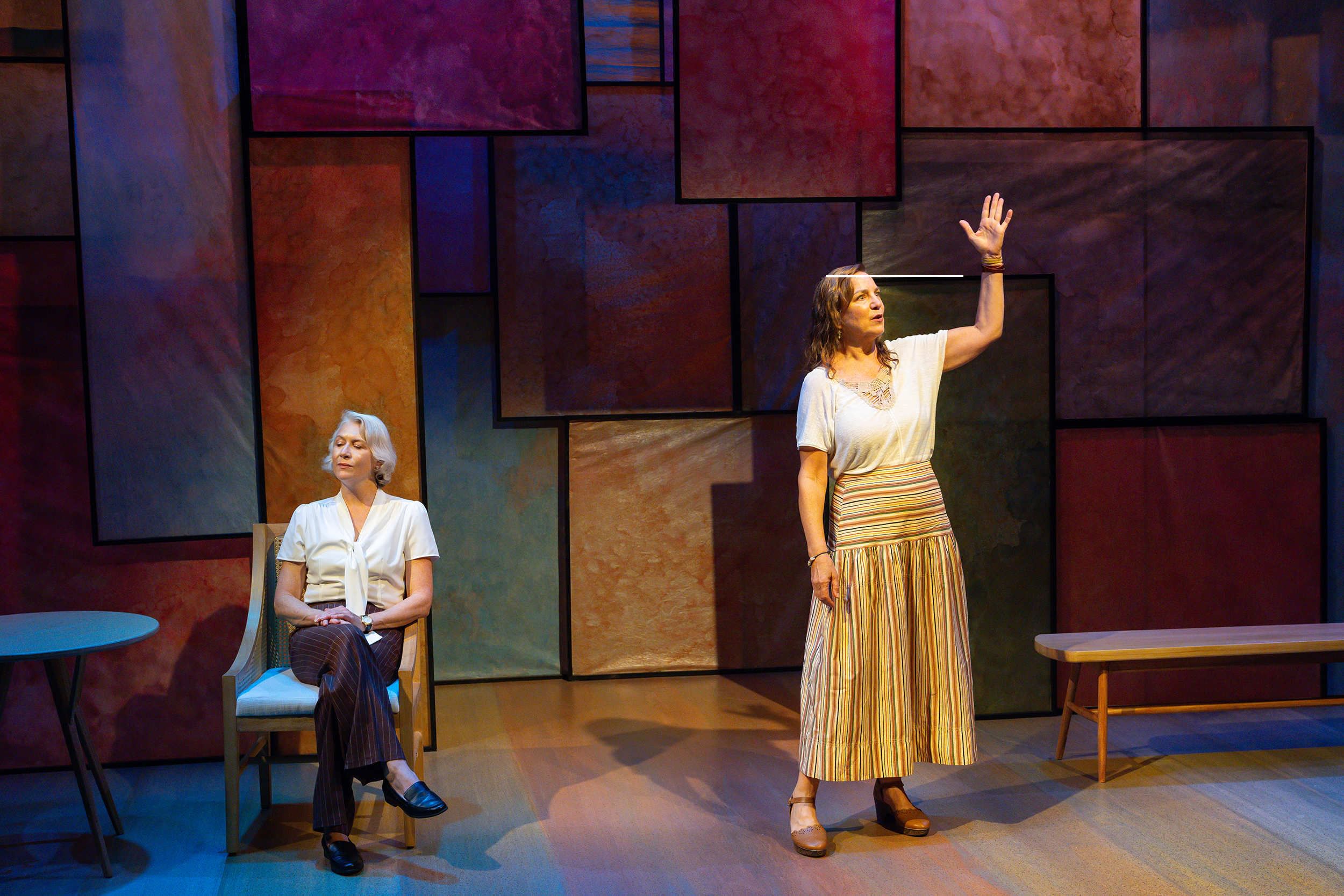 Kerrigan, a white-haired woman, sits at haughtily at left. Gonglewski, in a striped skirt, stands gesturing up with one hand