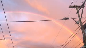 A huge, bright rainbow against a luminous peachy sunset sky over South Philly rowhouses.
