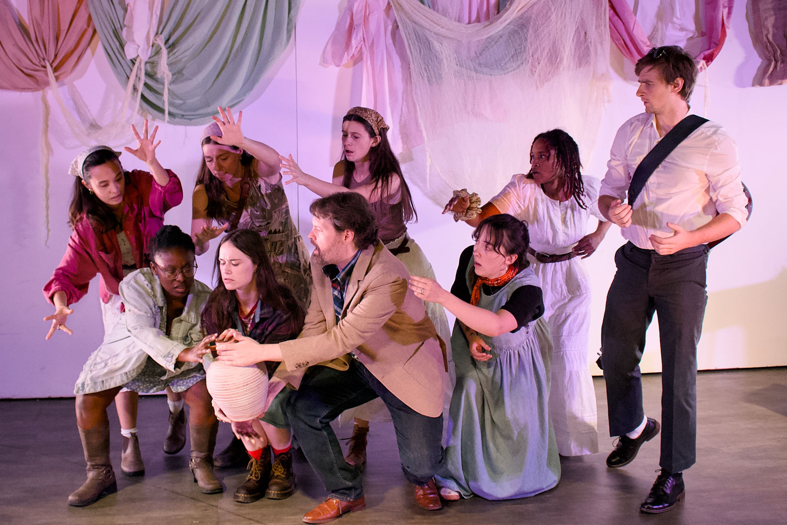 In a variety of clothes in neutral tones, the cast poses in anxious gestures toward a large clay pot held at bottom left.