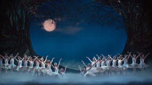 Several dancers in white tutus pose with arms and hands out, fog on stage, a backdrop with trees and a full moon, velvet sky