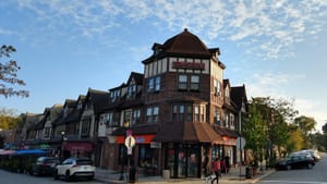 A street corner with a store front and Victorian rowhomes underneath a partly cloudy sky in Swarthmore.