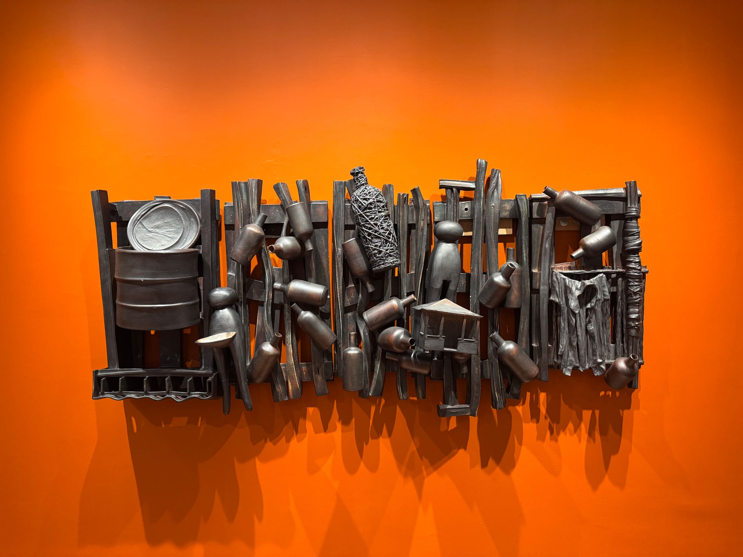 Rectangular wall piece with dynamic crowd of slats, tiny bottles, structures & clothespins, with dark, earthy graphite finish