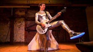 Bonetti, a white man in tight silver bodysuit and light-up sneakers, kicks one foot in the air as he plays an electric guitar