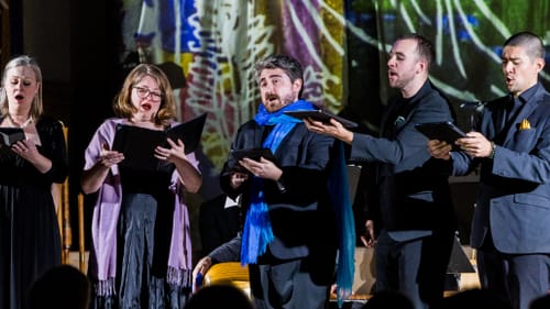 Two female singers and three male singers, with Perry at center wearing a long sky-blue scarf, sing on the chancel.