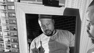 Crisp, richly saturated black & white photo of Ray looking in a mirror, holding a chess piece that casts dramatic shadows