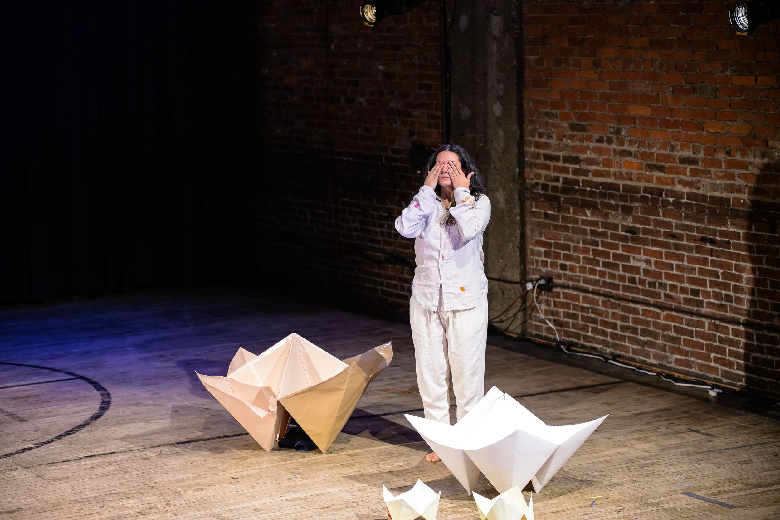 Sazak, with long dark hair, wears loose white clothes and covers their eyes, by big origami-style paper fortune tellers