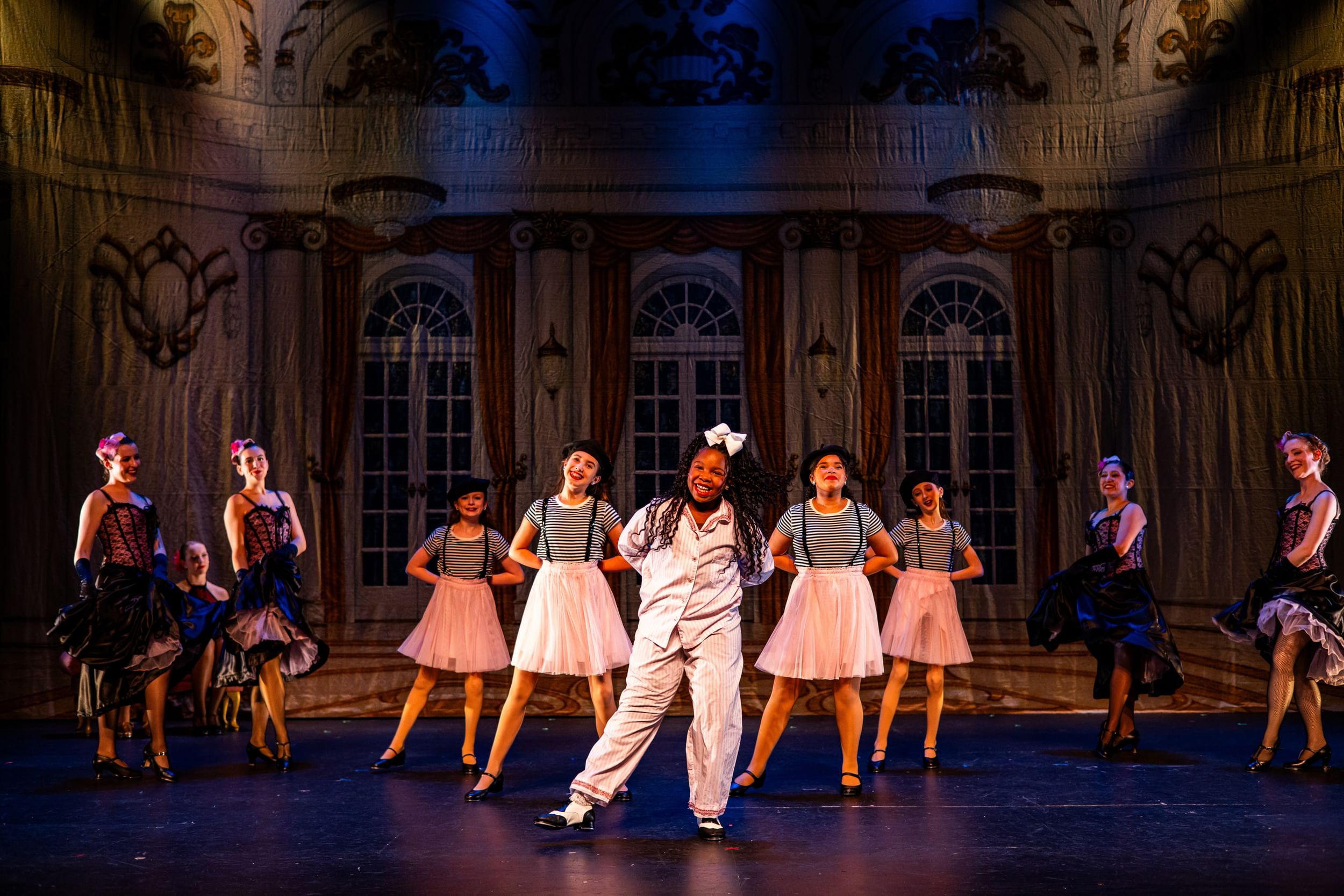 Five youth dancers are center stage, four adult dancers at opposite ends of stage. A muslin wall that look like a ball hall