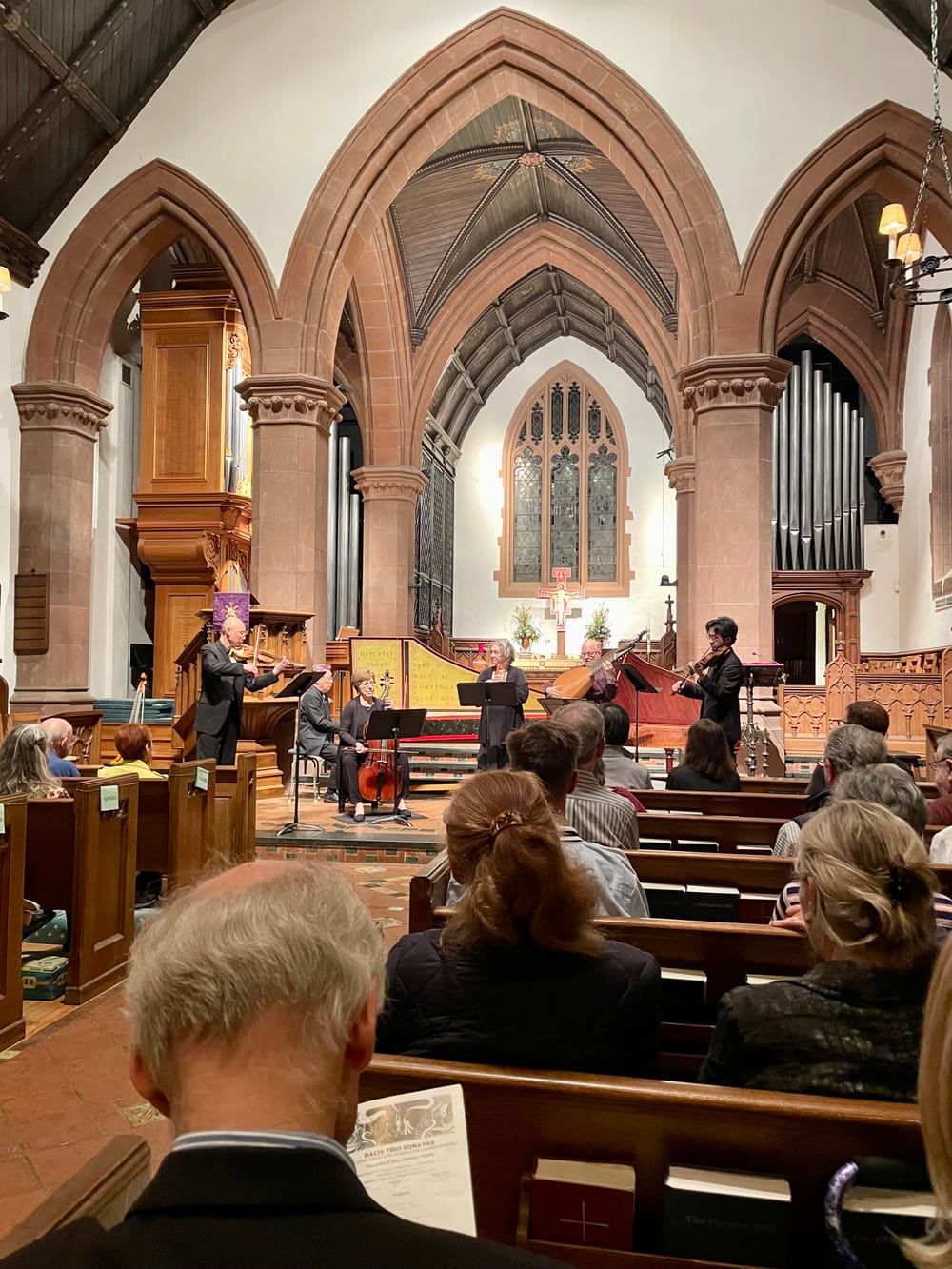 View from the audience in the church pews of six musicians playing period instruments on the chancel.