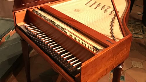 Close-up on the small, piano-like lautenwerck with its top open. It has a luxe natural-hued wooden frame and dark keys.