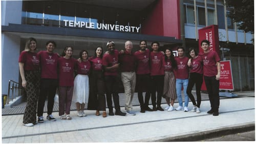 With a white man at center, a multiracial group of 12 students stand smiling in a line with their arms around each other