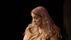 Breen, a white woman with blond hair wearing a gold top, sits and speaks with her hands folded in her lap.