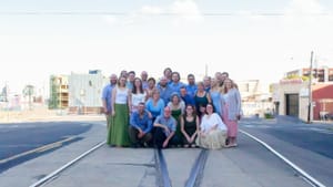 Members of the Crossing stand in the street by trolley tracks for a group photo on a sunny day