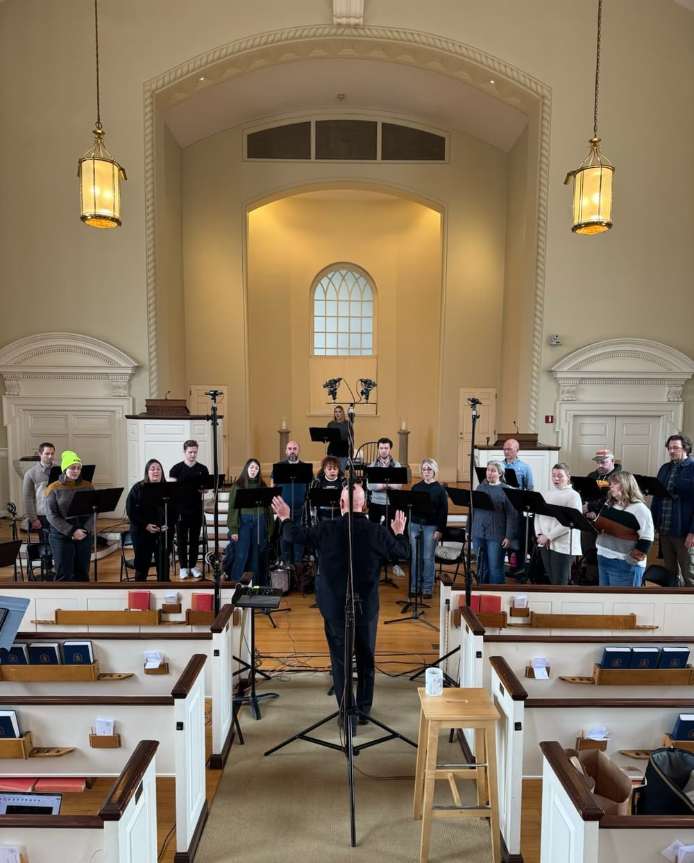 Nally, facing a choir of 16 standing on a church’s white chancel, conducts the singers in a rehearsal.