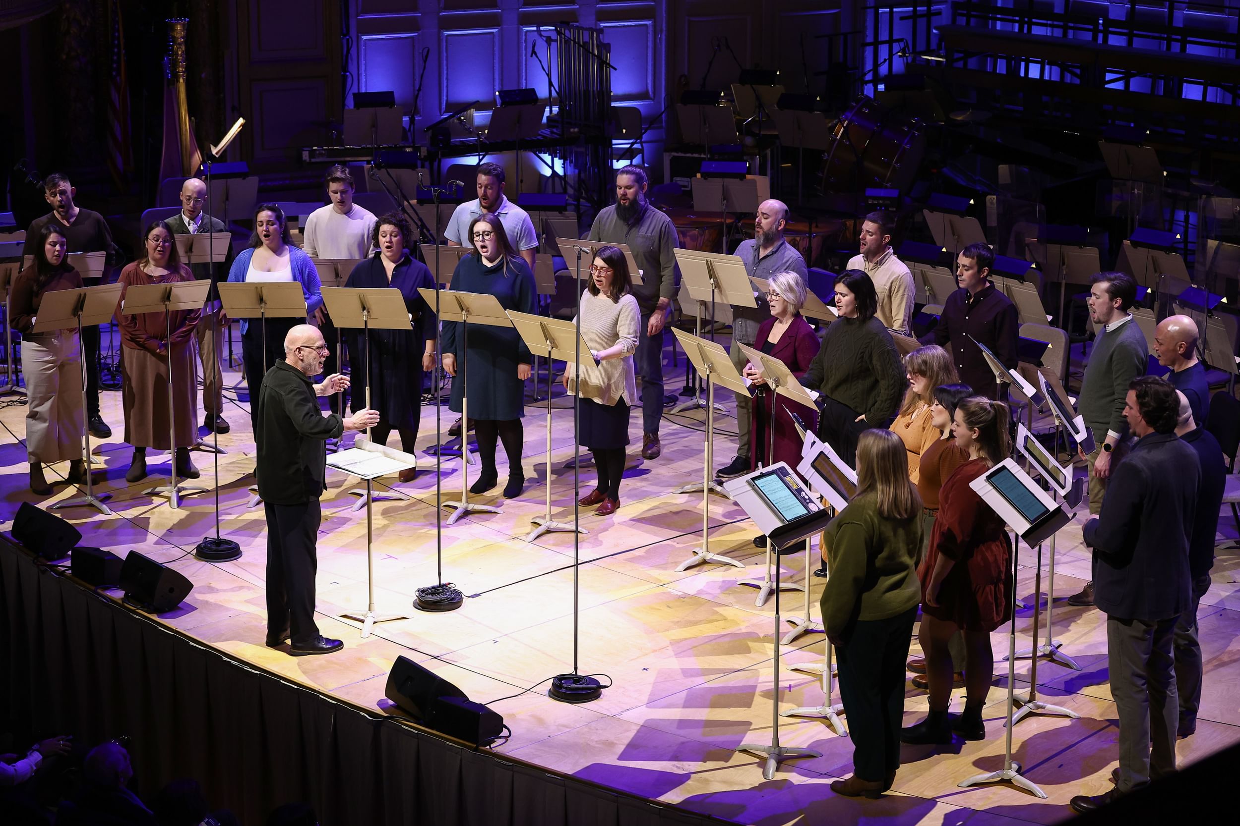 24 singers stand in two rows, women in front and men behind, around conductor Donald Nally at center.