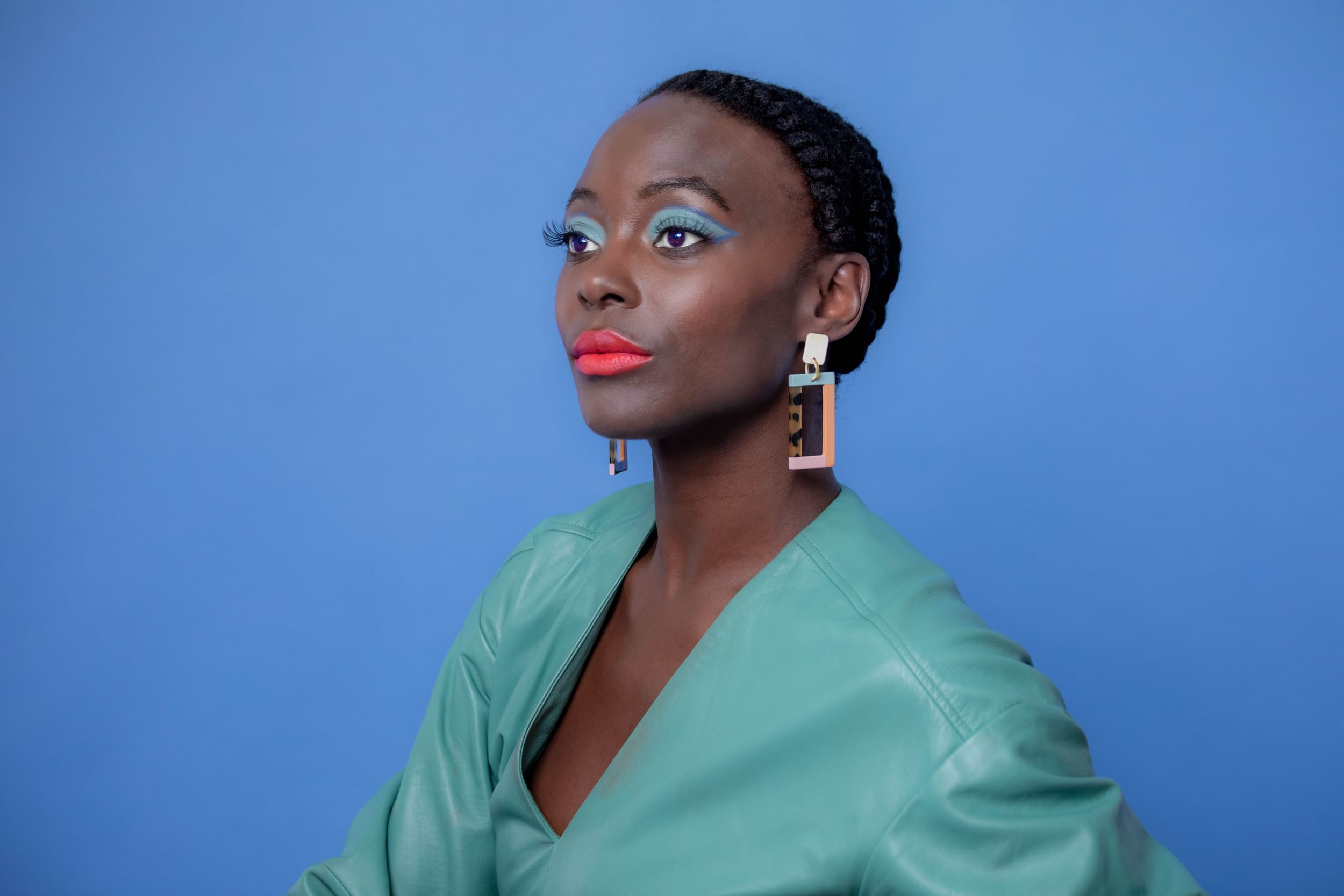 Closeup on Joachim from the shoulders up, a Black woman with a blue leather shirt, matching eyeshadow, and coral lipstick.