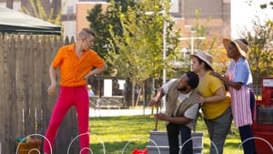 Vernal Belch, played by Pax Ressler in orange shirt and pink pants, intimidates three other characters on a stage in a park.