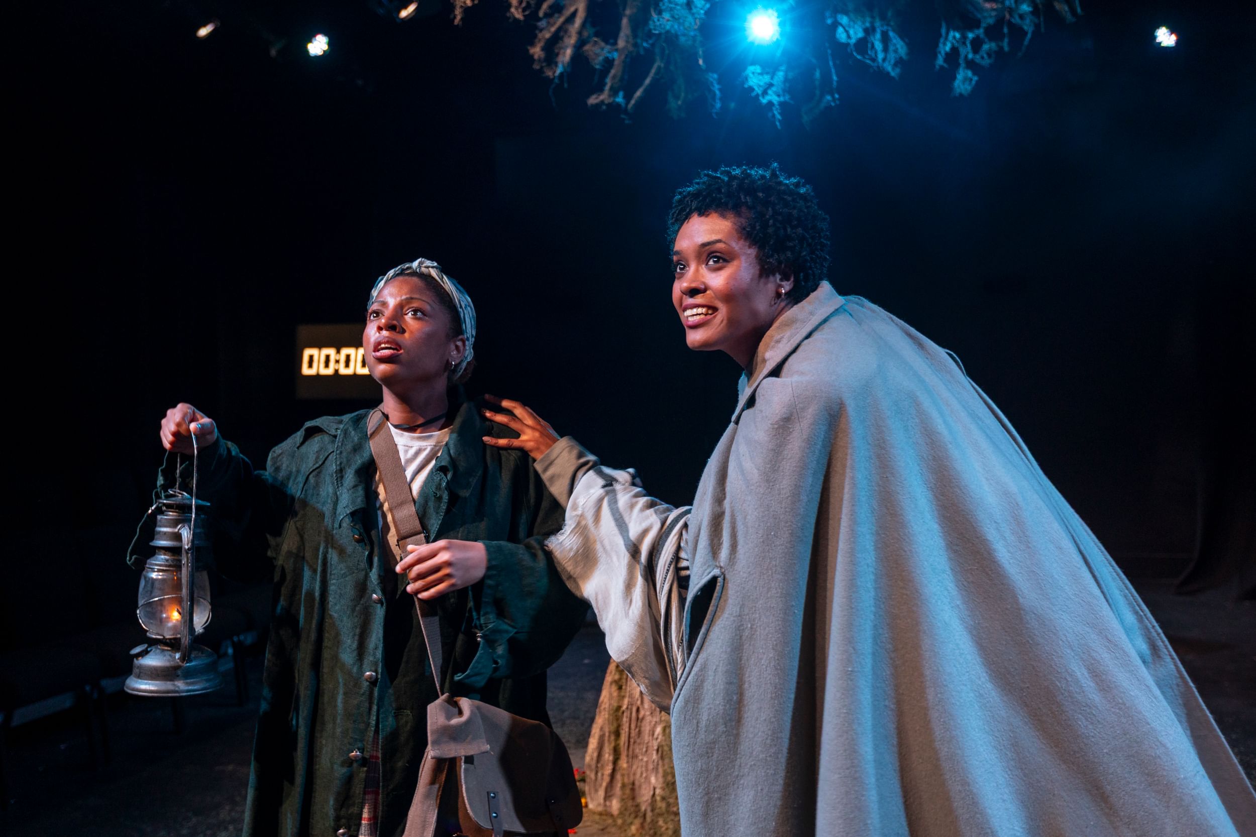 Murphy holds a 19th-century lantern while Rayne, in a long gray cape, touches her shoulder. They look outward anxiously.
