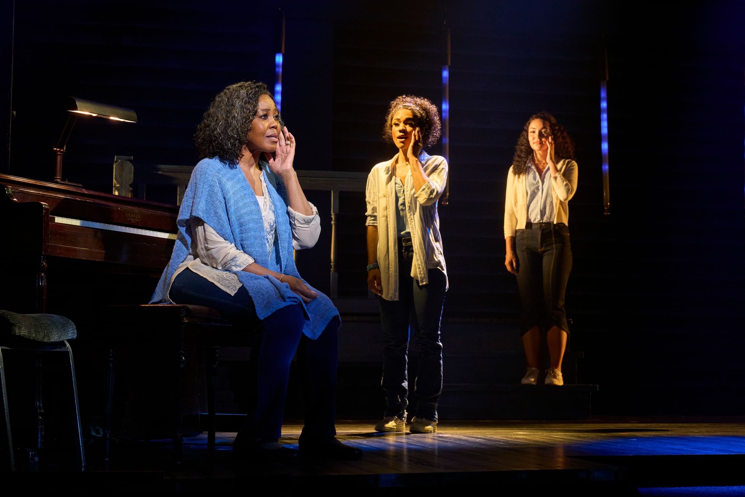 In the foreground, Brown, an older Black woman, touches her face while the two young women echo the gesture in the background