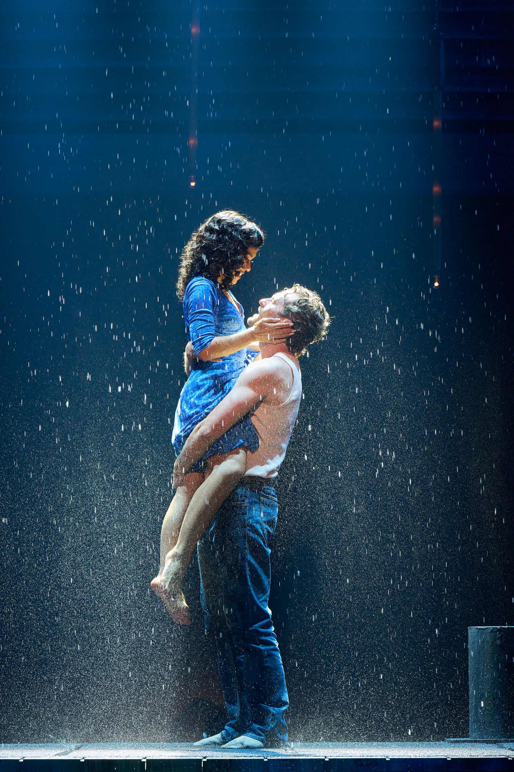 Seen in profile onstage in an atmospheric rain, Clark lifts Deslorieux up passionately while she touches his face.