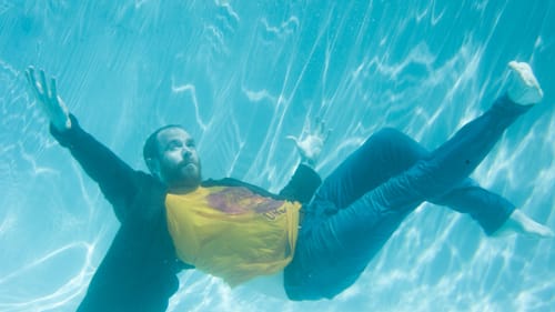Davis, limbs spread out, seen from underwater as he sinks to the bottom of a pool with all of his clothes on.