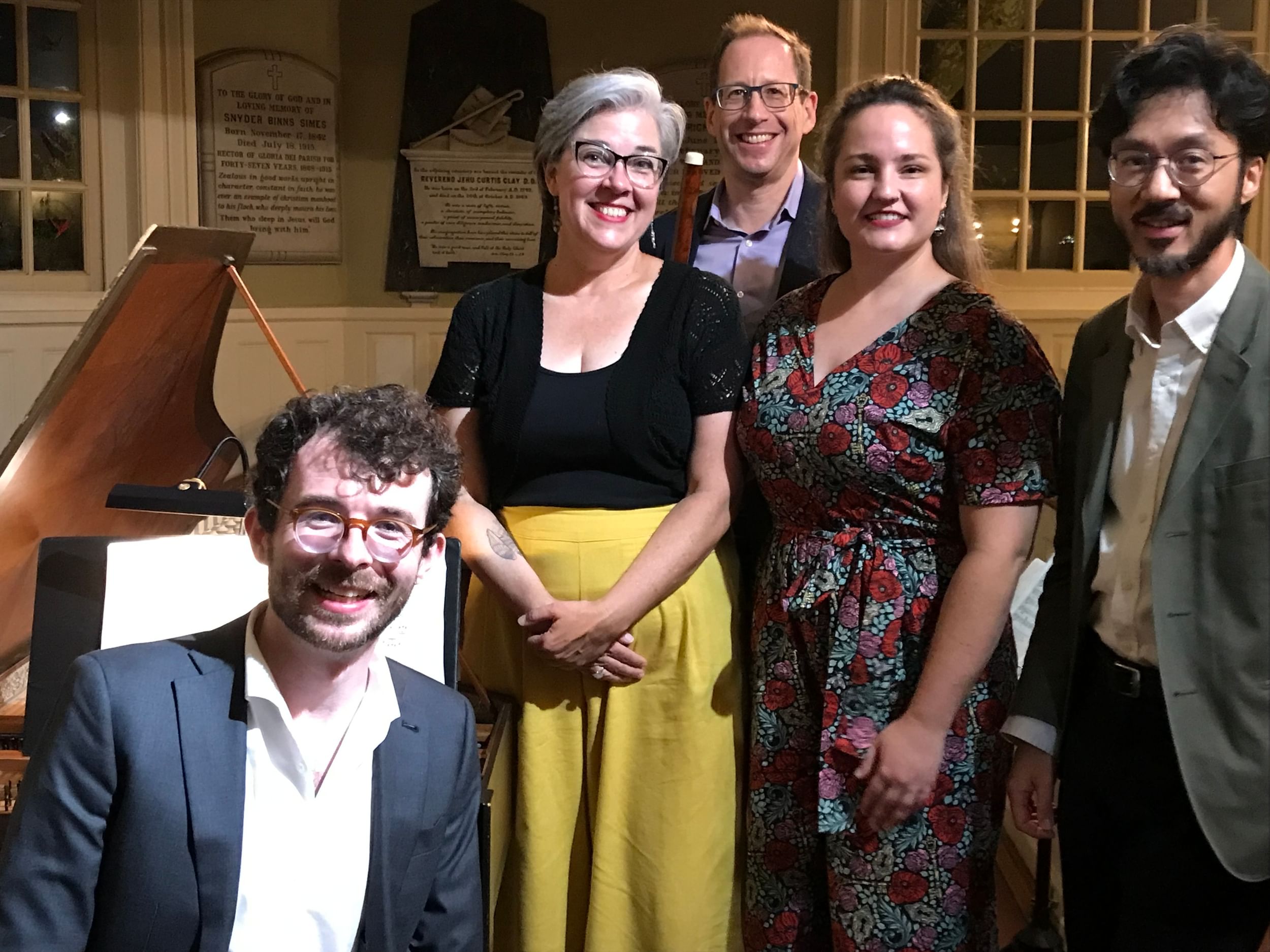 Five people gather by a grand piano, posing for a portrait
