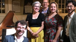 Five people gather by a grand piano, posing for a portrait