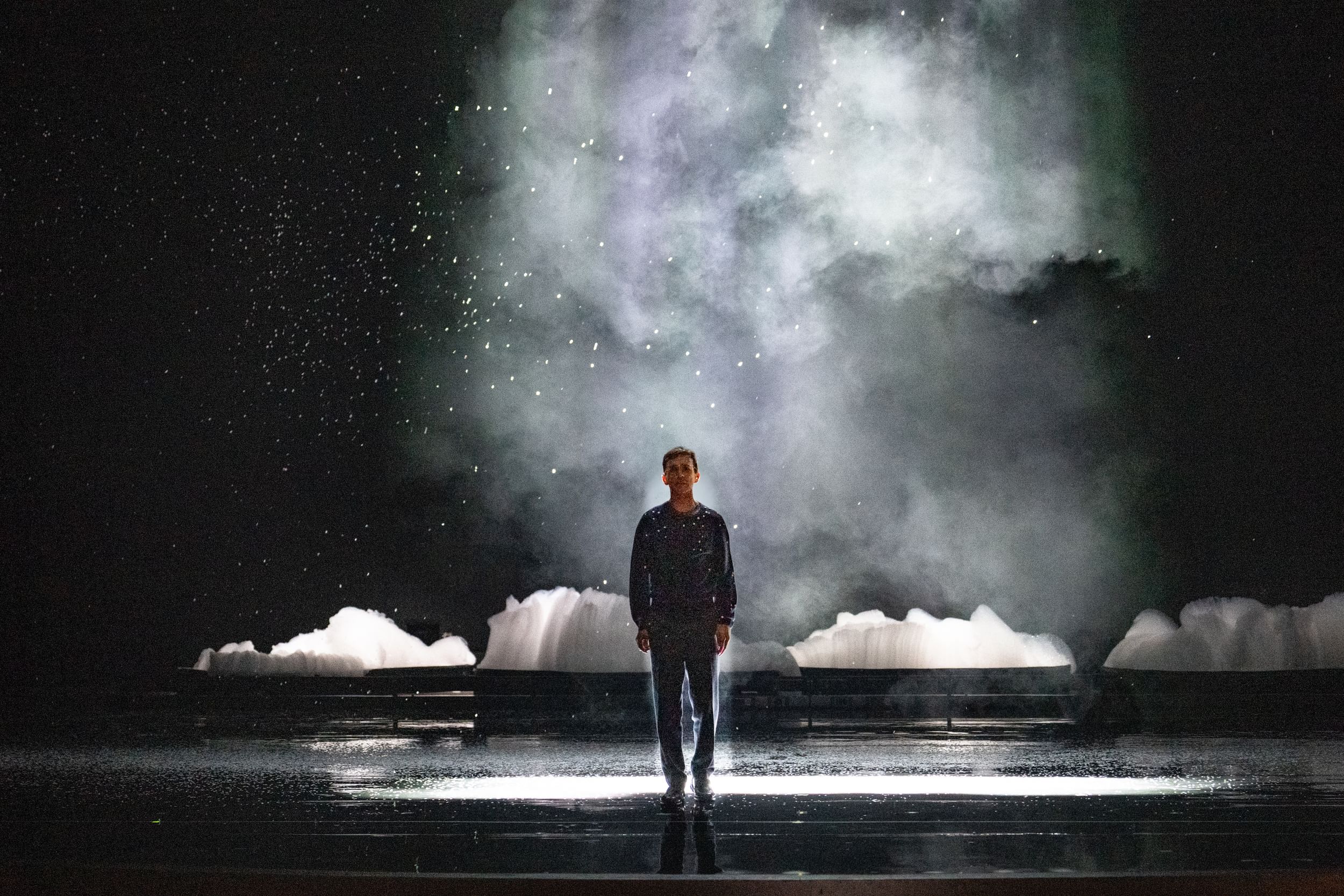 Costanzo, small and alone onstage, stands in a dramatic misty swath of light and snow, mountains of soap bubbles behind him.