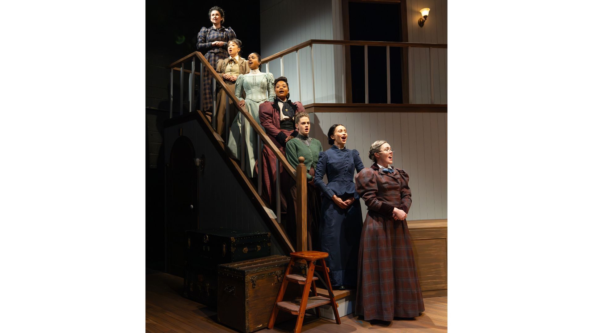 The multiracial cast of women, in sober floor-length, long-sleeved 19th-century dresses, stand on a staircase singing.