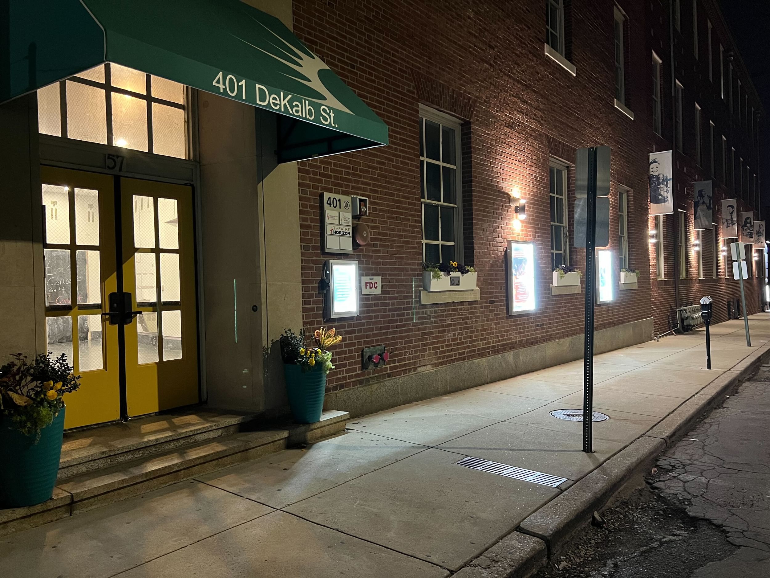 Nighttime view of a large brick building with a yellow door and green awning over it.