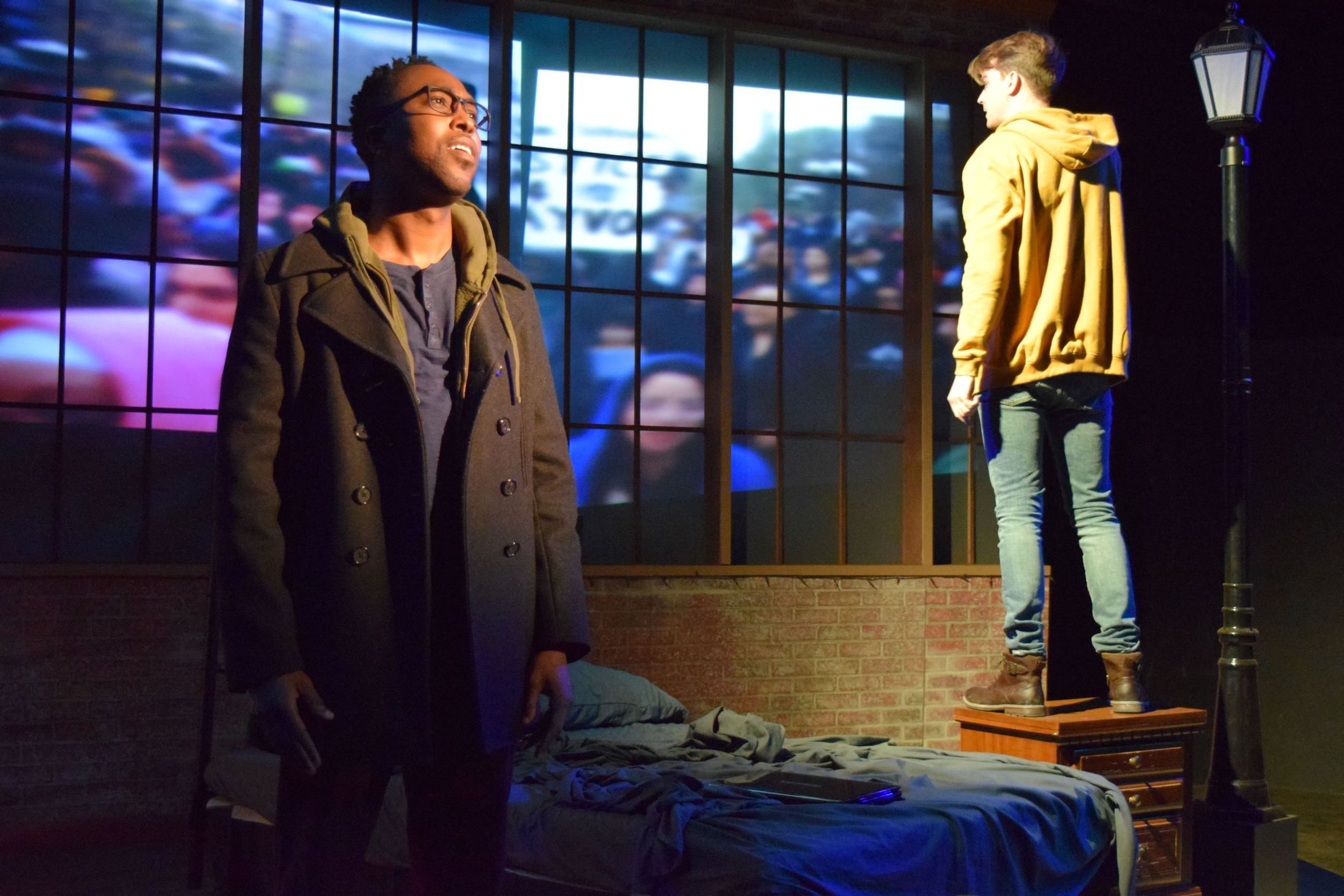 A scene from the play: David Bazemore & Gabriel Elmore face away from each other in a bedroom with brick walls & large window