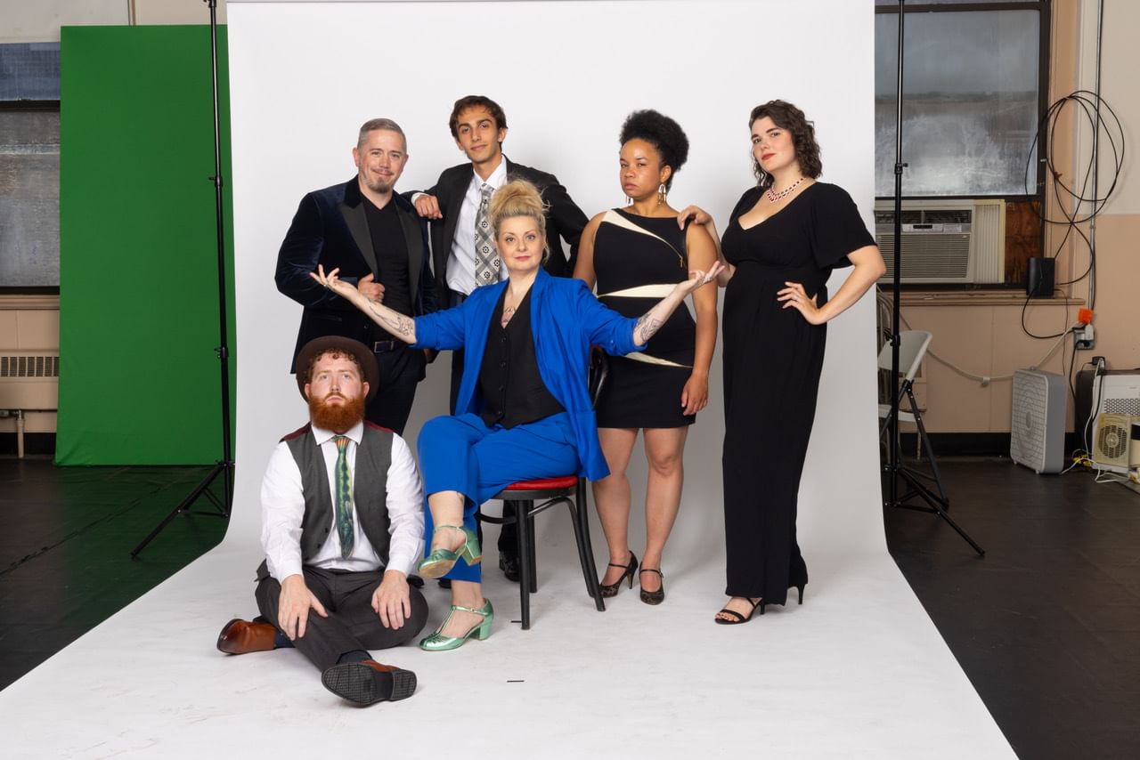 Six diverse people, in contemporary evening wear, pose together in a studio with a white paper backdrop.