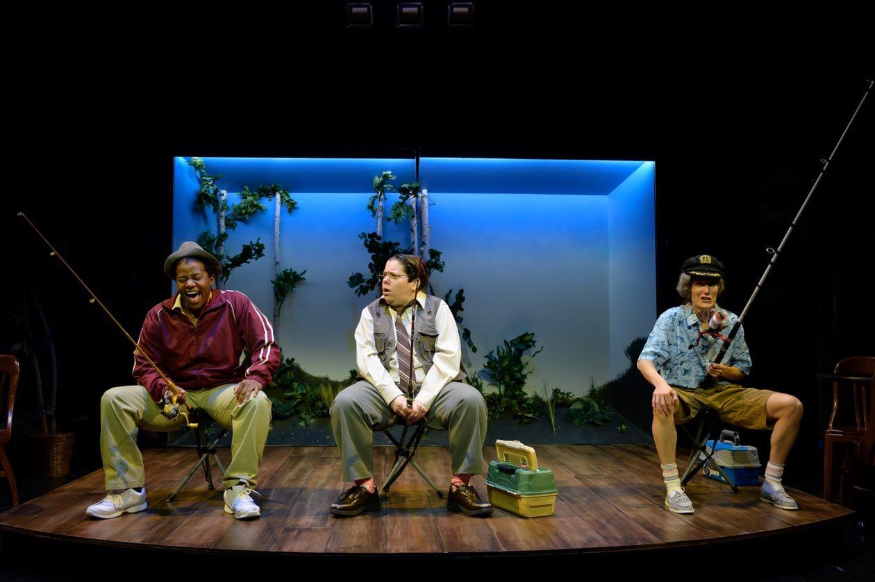 The three actors play elderly male fishermen, sitting on portable stools and holding large fishing poles between their legs.