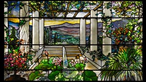 Richly colored, detailed view of a garden with white pillars, a golden mountain sunset in the distance, all in stained glass