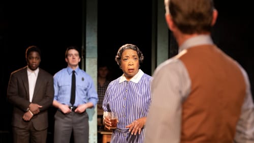 Atticus, seen from behind, faces Calpurnia, in a blue-striped dress, & Tom Robinson, who stands by a white police officer