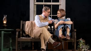 Atticus, with gray hair and a tan suit, speaks to Scout, with short brown hair and denim overalls. She looks worried.