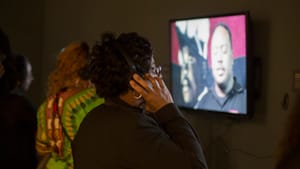 At the exhibition's opening reception, a viewer watches one of Scribe's videos. (Photo by Meredith Edlow)