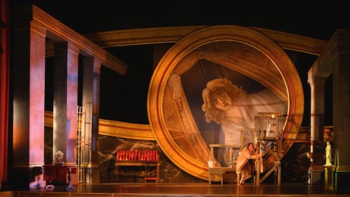 A large, architecturally arresting opera set featuring a circle 20+ feet high framing a giant, tilted painting of a sad woman