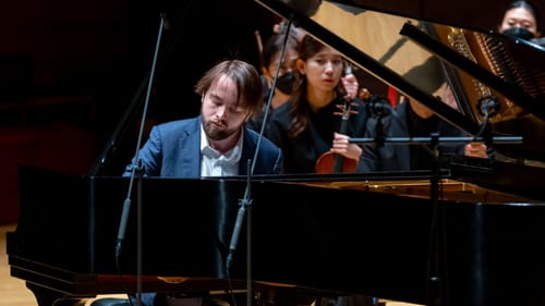 Trifonov, a 31-year-old white man with straight brown hair, plays the grand piano with a look of concentration.