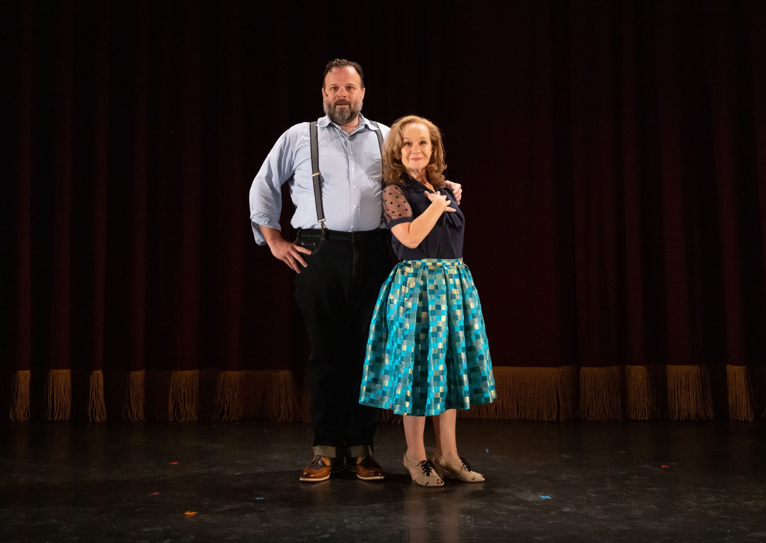 Childs stands in front to the left of Greer on stage, looking towards camera, the curtain down behind them