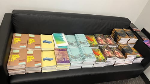 A low black couch stacked with dozens of copies of 8 different issues of the UArts student lit mag.