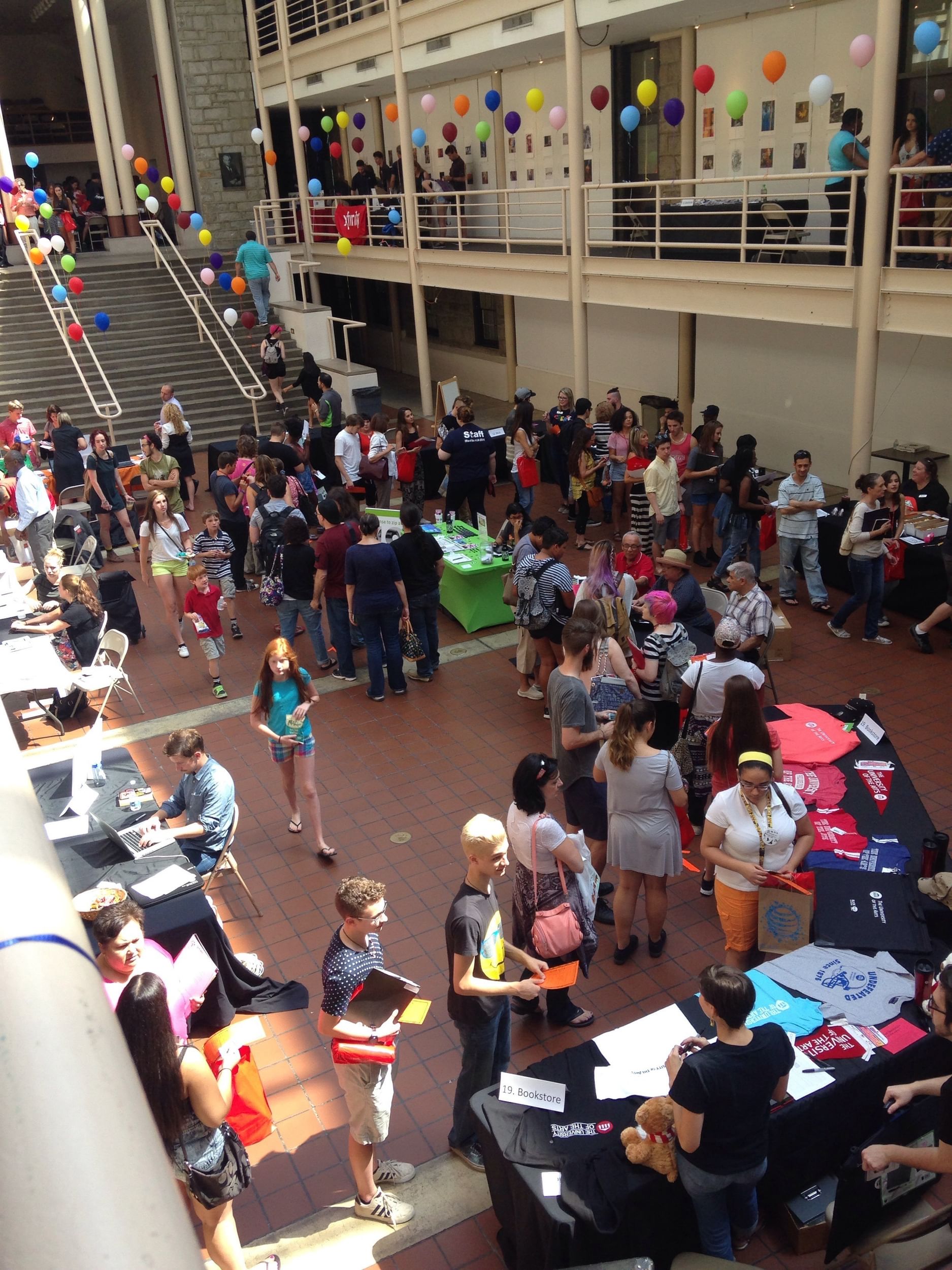 View from the mezzanine of a hall crowded with students and vendor tables, balloons decorating the central stairway.