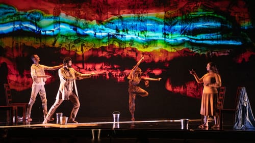 Under a graphically complex rainbow-hued projection, the singers face each other as Dolphin dances at center.