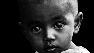 Close-up high-contrast black & white photo of an Indian toddler with huge eyes and plaintive expression.