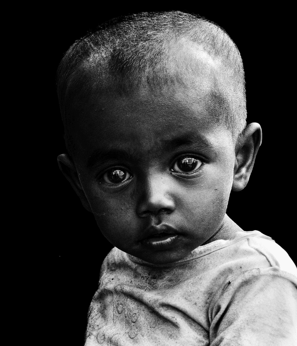 Close-up high-contrast black & white photo of an Indian toddler with huge eyes and plaintive expression.