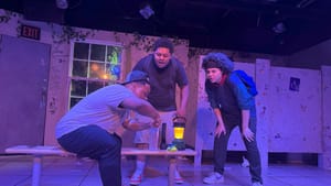 Three teenage boys crowd around a bench in a run-down school bathroom, washed in blue light.